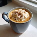 Zbliżenie na kubek domowego Pumpkin Spice Latte ze śmietaną i cynamonem.