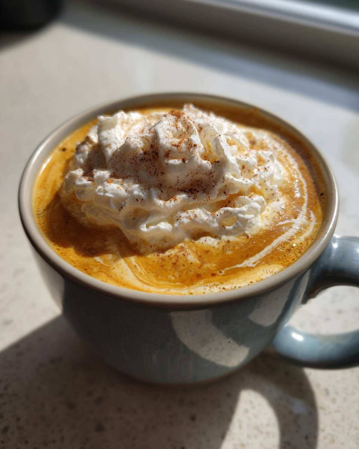 Zbliżenie na kubek domowego Pumpkin Spice Latte z bitą śmietaną i cynamonem.