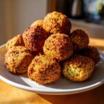 Stos pysznego falafela pieczonego na białym talerzu, z widocznym jednym kawałkiem.