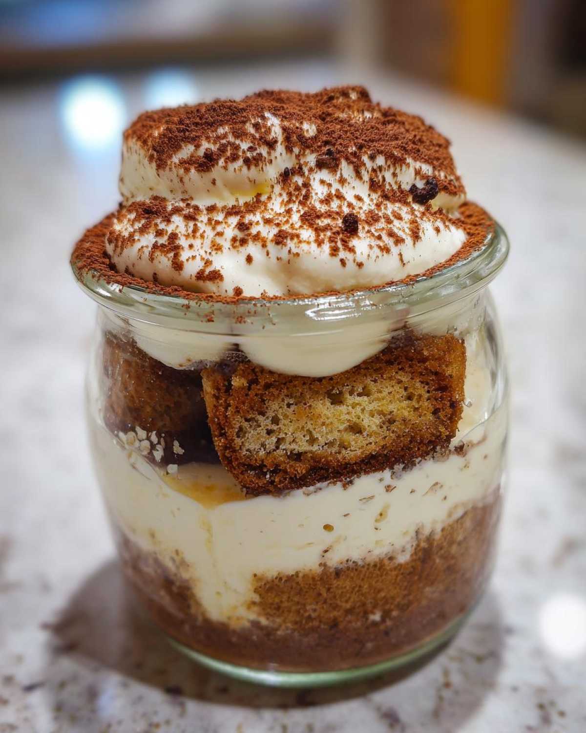 Warstwowe fit tiramisu bez cukru w szklanym słoiczku, przełożone biszkoptami i kremem, posypane kakao.