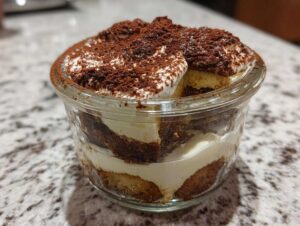 Zbliżenie na warstwowe fit tiramisu bez cukru w szklanej miseczce, posypane kakao.