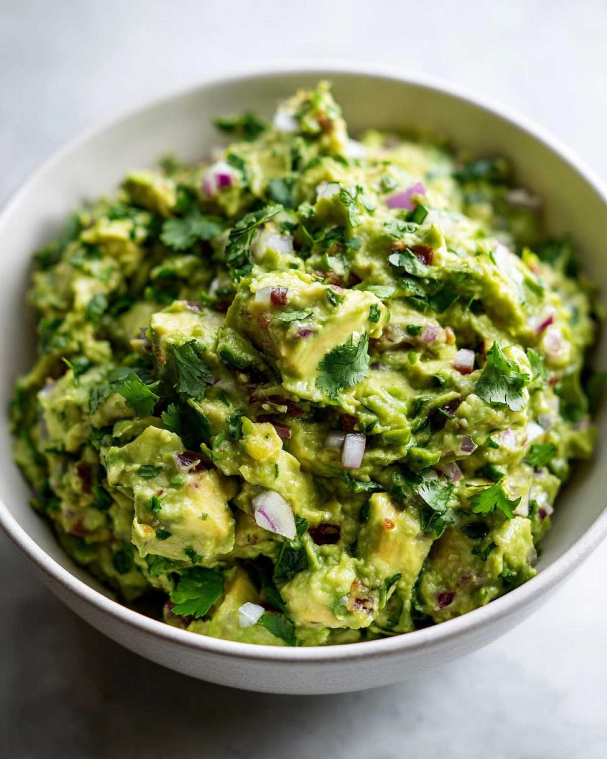 Miska pełna świeżego, domowego guacamole z kawałkami awokado, cebuli i kolendry.