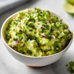 Miseczka pełna pysznego guacamole domowego, posypanego świeżą kolendrą i kawałkami czerwonej cebuli.