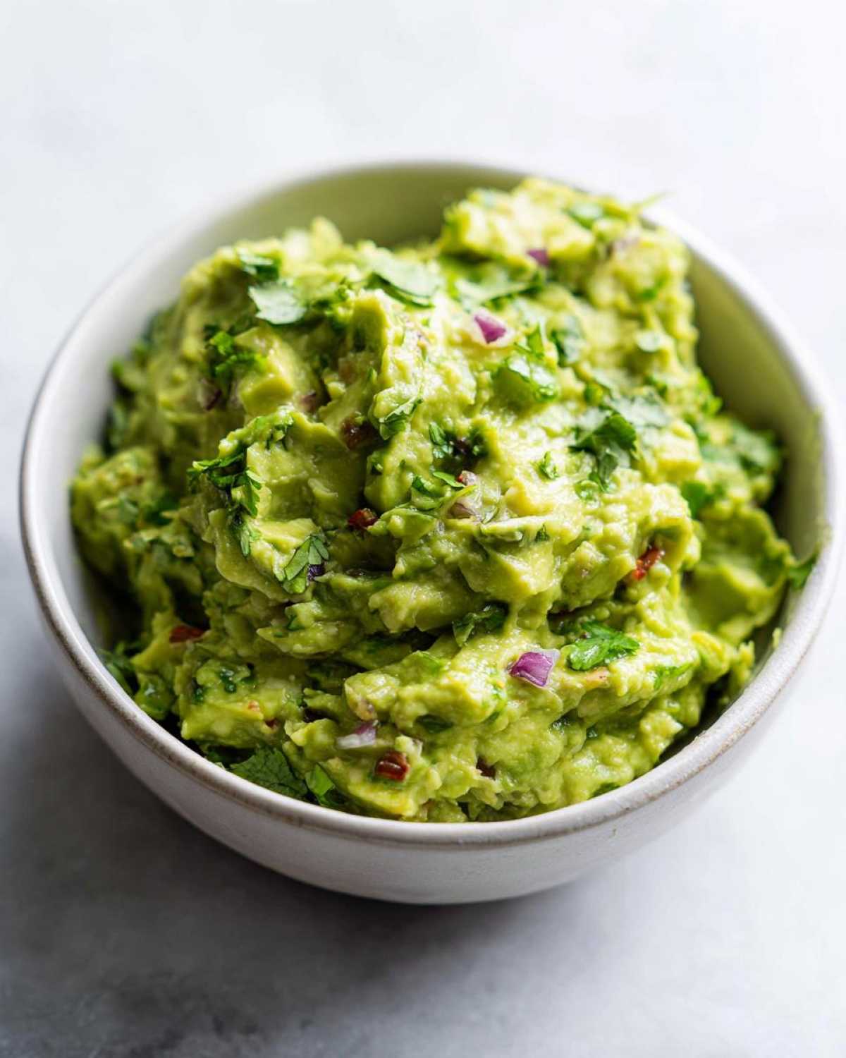 Miseczka pełna pysznego, domowego guacamole z kawałkami awokado, kolendry i czerwonej cebuli.