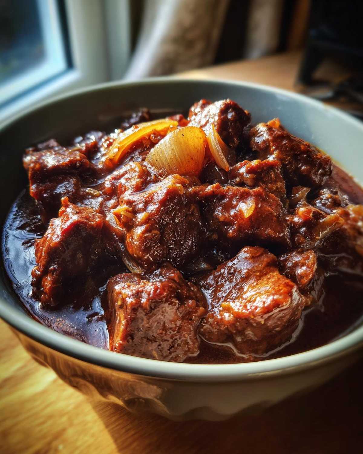 Zbliżenie na miskę pełną tradycyjnego gulaszu wołowego z kawałkami mięsa i cebuli w sosie.