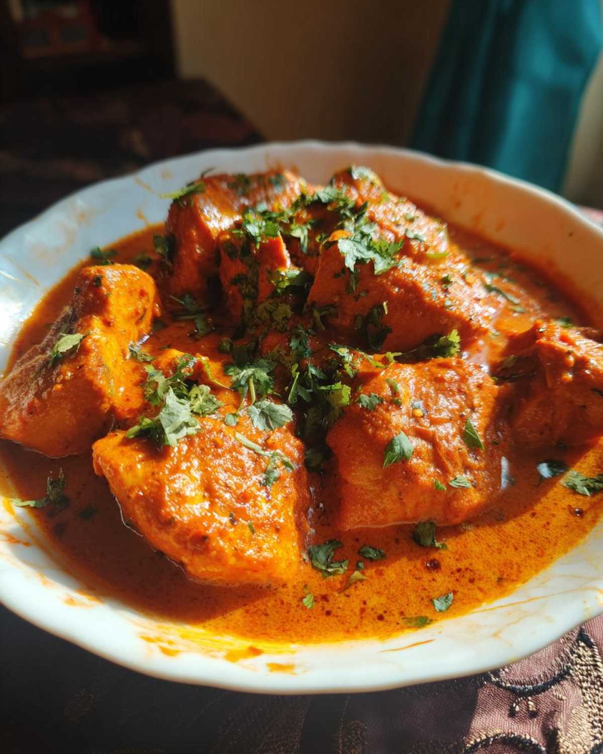 Zbliżenie na miskę z kurczakiem tikka masala, polany kremowym, pomarańczowym sosem i posypany świeżą kolendrą.