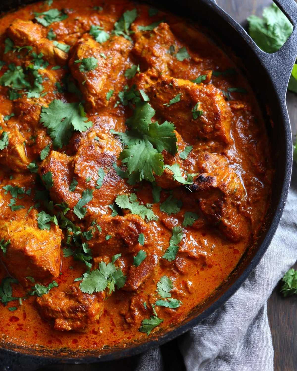 Zbliżenie na kurczaka tikka masala w kremowym, pomarańczowym sosie, udekorowanego świeżą kolendrą.