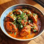 Miseczka pełna aromatycznego kurczaka tikka masala, udekorowana świeżą natką pietruszki.