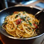 Zbliżenie na talerz z makaronem aglio e olio, udekorowanym pomidorkami koktajlowymi i świeżą bazylią, posypany parmezanem.