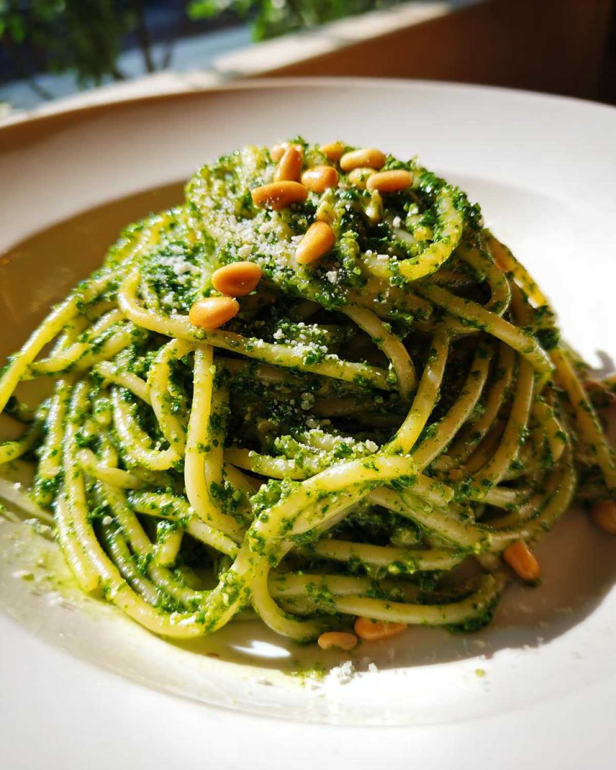 Makaron z pesto bazyliowym, posypany parmezanem i orzeszkami pinii, na białym talerzu.