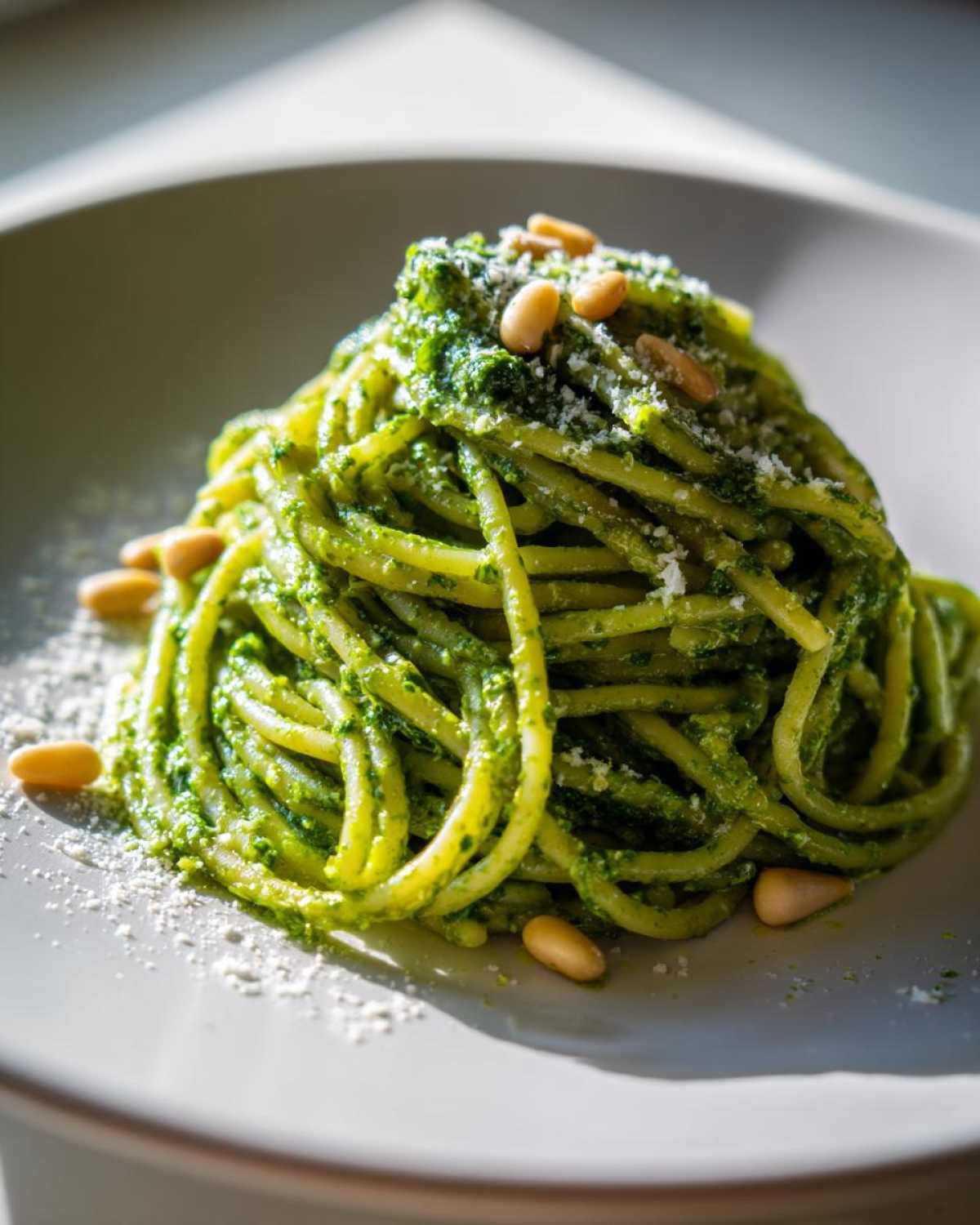Zbliżenie na talerz z makaronem z pesto bazyliowym, posypany parmezanem i orzeszkami pinii.