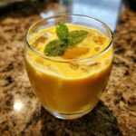 Szklanka orzeźwiającego mango lassi koktajlu indyjskiego z lodem i listkami mięty na wierzchu.