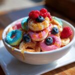 Miseczka pełna kolorowych mini naleśników z TikToka pancake cereal, polanych syropem i ozdobionych malinami i borówkami.
