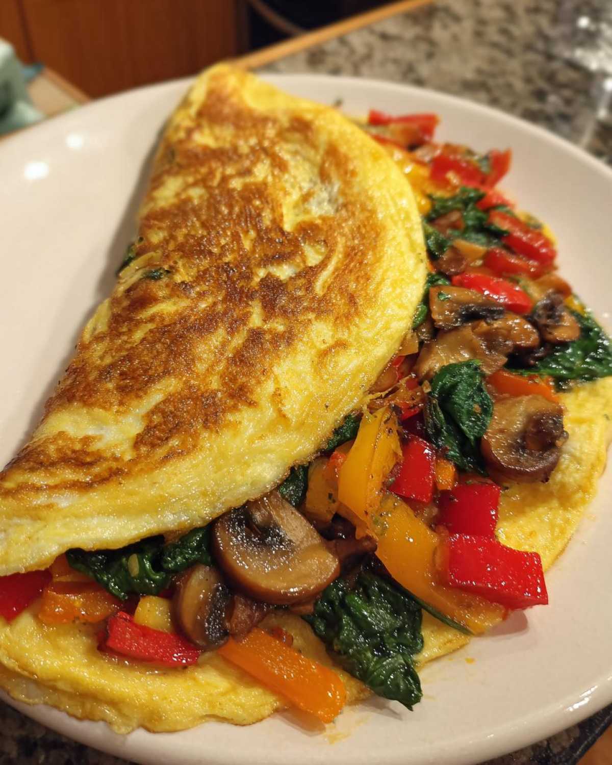 Gotowy omlet białkowy z warzywami, zawierający paprykę, szpinak i pieczarki, na białym talerzu.
