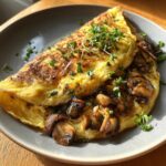 Złocisty, puszysty omlet z pieczarkami, udekorowany świeżymi ziołami.