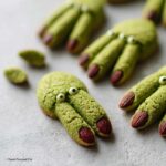 Zielone ciasteczka w kształcie palców wiedźmy z migdałami jako paznokciami, idealne na Halloween.