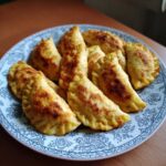Talerz pełen złocistych, smażonych pierogów leniwych, ułożonych na wzorzystym talerzu.