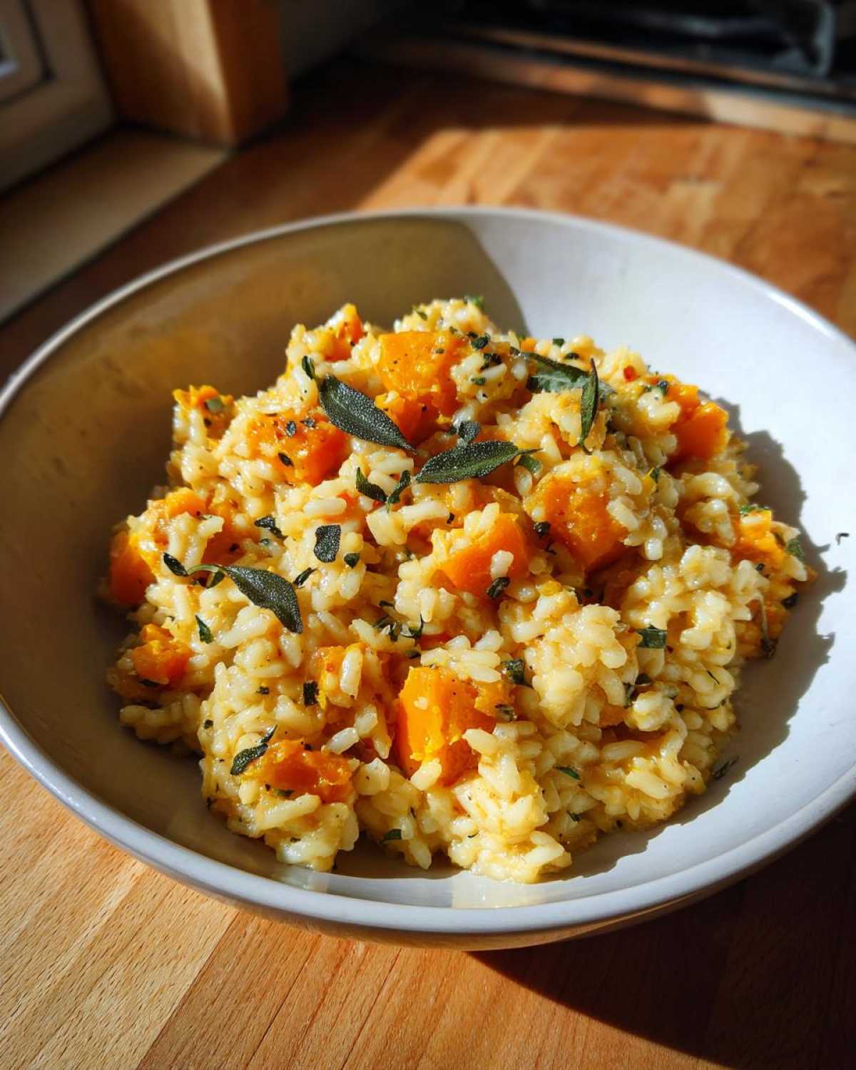 Miseczka kremowego risotto dyniowego z kawałkami dyni i listkami szałwii, gotowe do podania.
