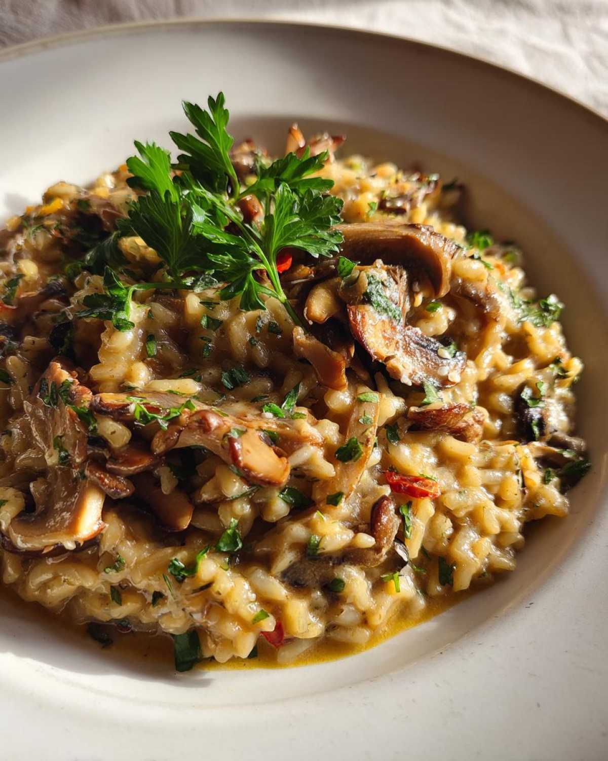 Zbliżenie na talerz z kremowym risotto z grzybami, udekorowane natką pietruszki.