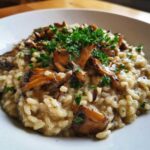 Zbliżenie na talerz z kremowym risotto z grzybami, posypane świeżą natką pietruszki.