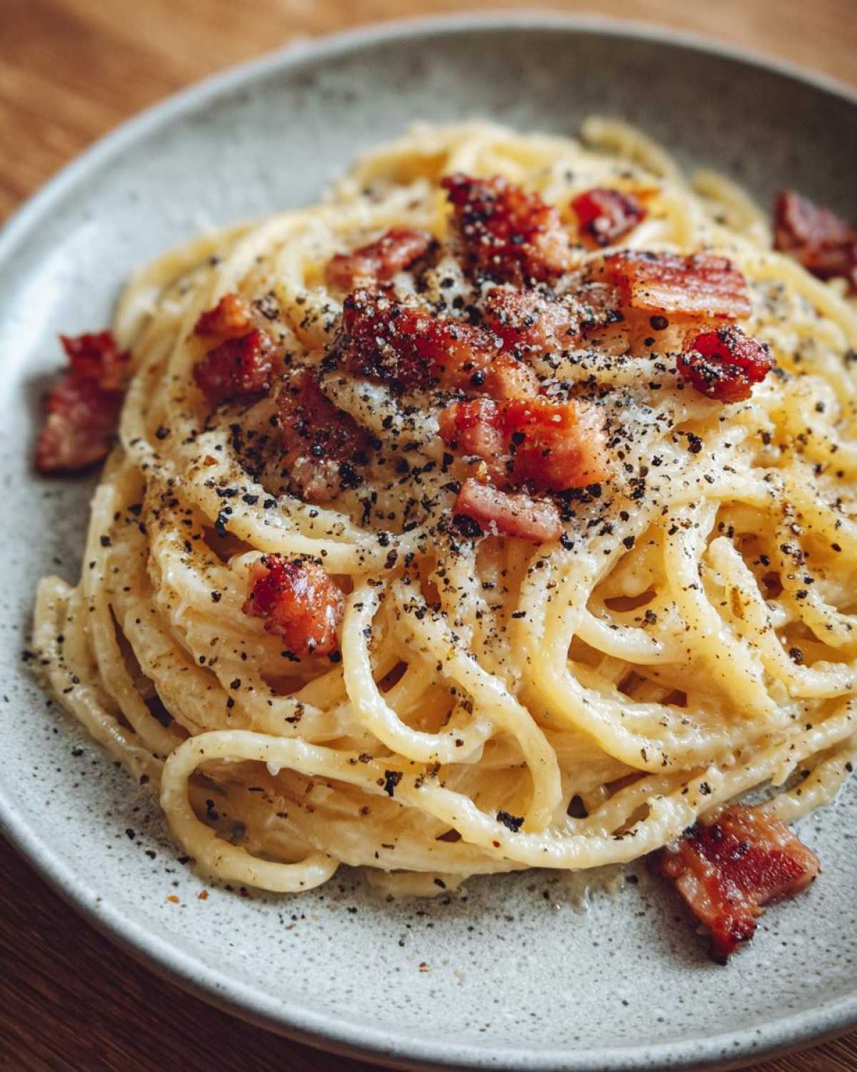 Zbliżenie na talerz spaghetti carbonara z chrupiącym boczkiem i świeżo mielonym pieprzem.