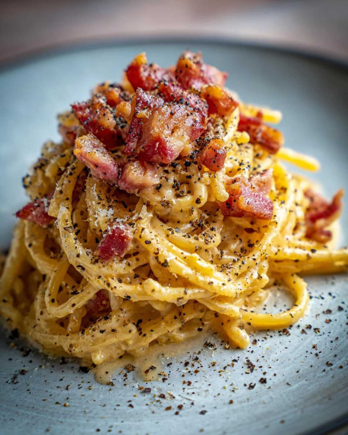 Zbliżenie na talerz spaghetti carbonara, udekorowane kawałkami chrupiącego guanciale i świeżo mielonym czarnym pieprzem.