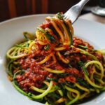 Widok z bliska na spaghetti z cukinii z bogatym sosem pomidorowym, nabrane na widelec.