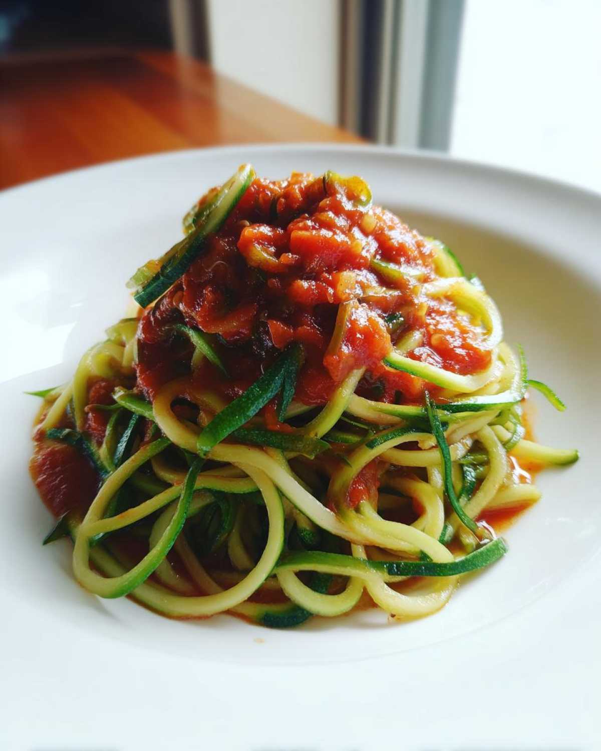 Spaghetti z cukinii z sosem pomidorowym na białym talerzu, danie z makaronu z cukinii.