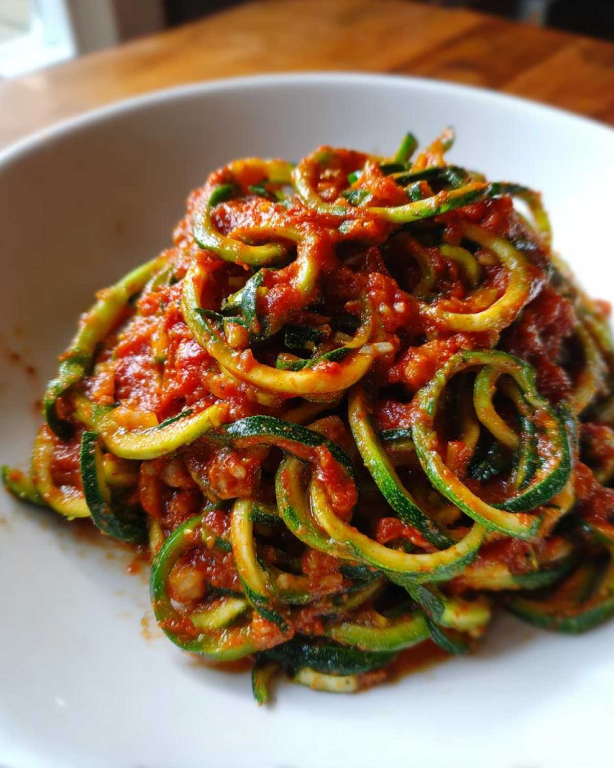 Spaghetti z cukinii z sosem pomidorowym w białej misce, danie z makaronu z cukinii.