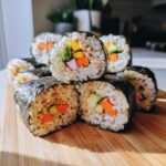 Zbliżenie na sushi maki z ryżem, nori i kolorowymi warzywami: marchewką, ogórkiem, papryką i brokułem.