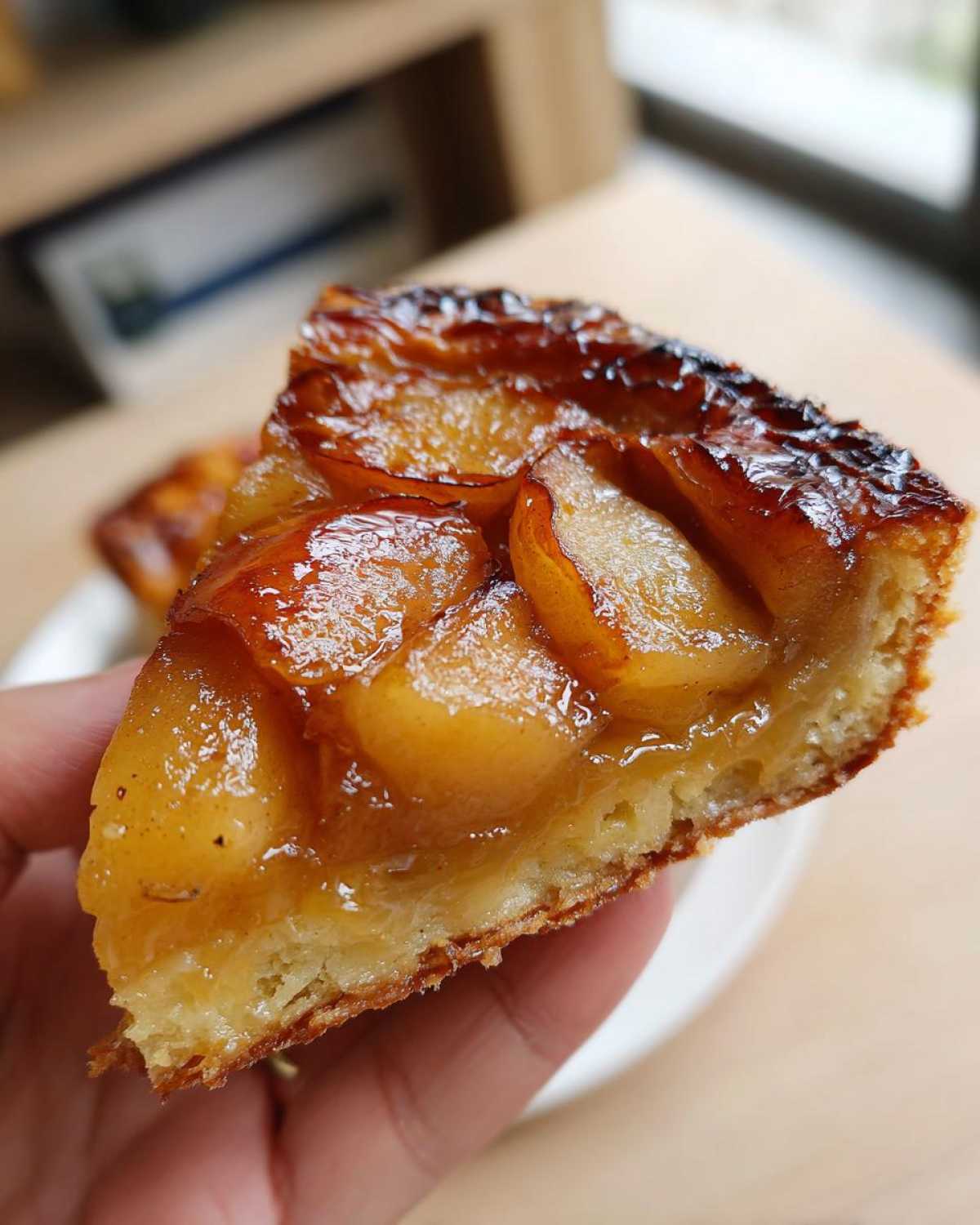 Kawałek przepysznej Tarty Tatin z karmelizowanymi jabłkami i kruchym ciastem, trzymany w dłoni.