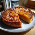 Kawałek przepysznej Tarta Tatin z karmelizowanymi jabłkami na szarym talerzu.