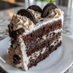Kawałek tortu Oreo z ciemnym biszkoptem, kremem i kawałkami ciastek, ozdobiony całymi ciastkami Oreo na wierzchu.