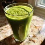 Szklanka zielonego koktajlu detoks na blacie, z widocznymi pęcherzykami na powierzchni.