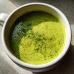 Zupa krem z brokułów light w białej filiżance, posypana ziołami.