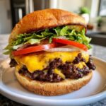 Soczysty burger wołowy domowy z podwójną porcją mięsa, roztopionym serem, sałatą, pomidorem i cebulą.