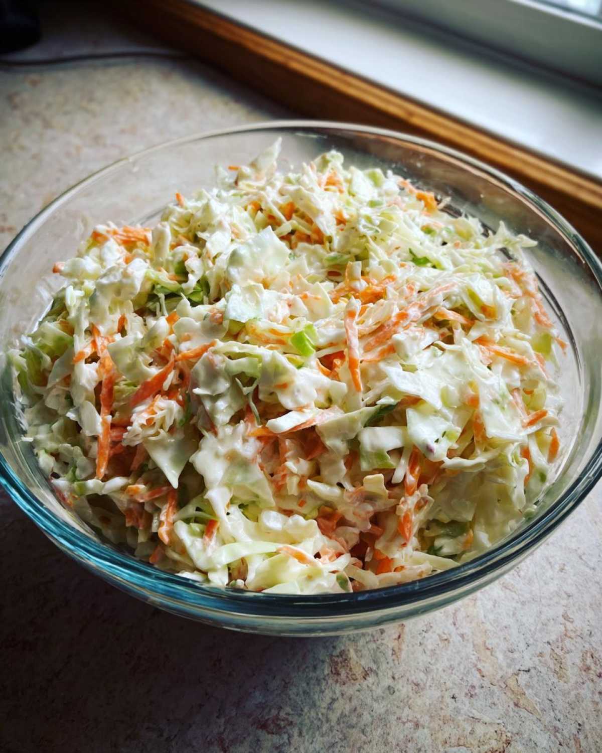 Zbliżenie na miskę pełną świeżego coleslaw domowy z poszatkowaną kapustą i marchewką w kremowym sosie.