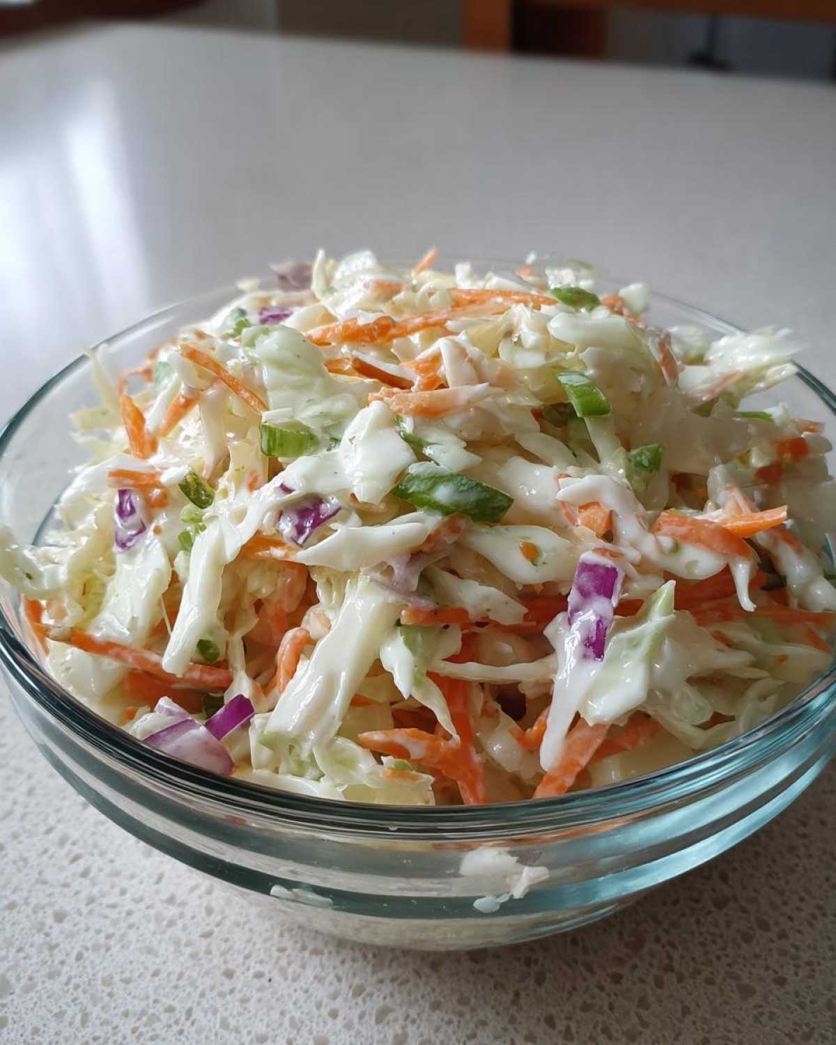 Szklana miska pełna świeżego coleslaw domowy z marchewką, cebulą i zieloną cebulką.