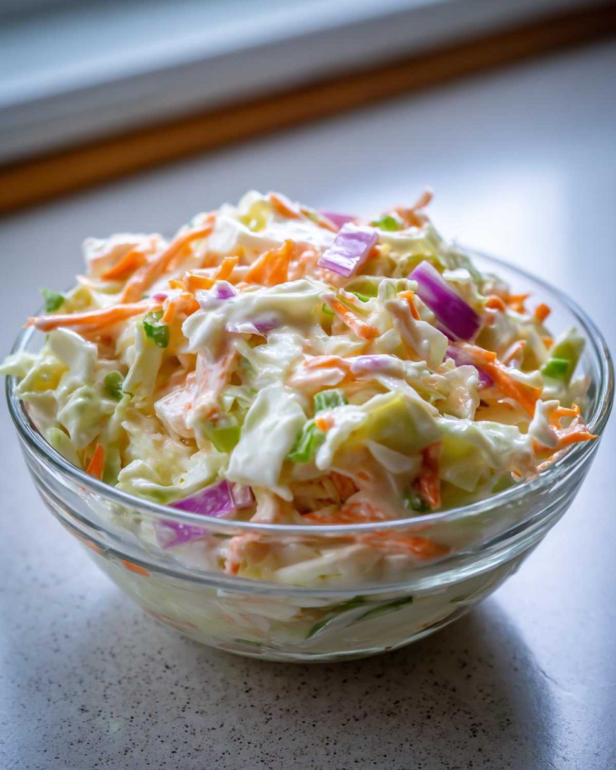 Szklana miska pełna świeżego coleslaw domowy z marchewką, kapustą i czerwoną cebulą.