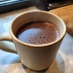 Gorąca czekolada w ceramicznym kubku, z widoczną parą unoszącą się nad pianką.
