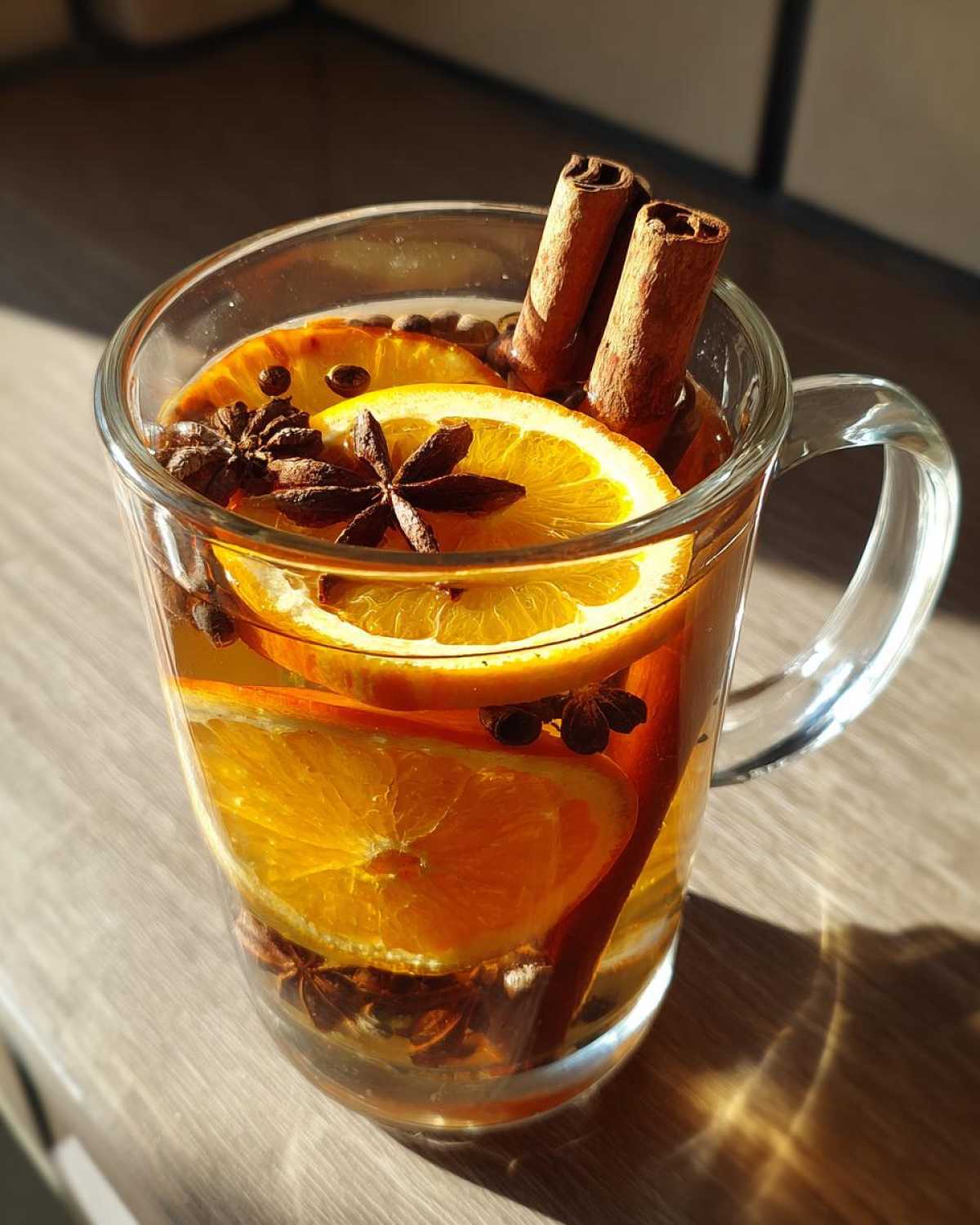Szklanka z aromatyczną herbatą zimową, ozdobiona plastrami pomarańczy, laskami cynamonu i gwiazdkami anyżu.
