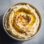 Zbliżenie na kremowy hummus z ciecierzycy polany oliwą i posypany papryką.