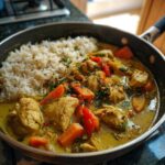 Zbliżenie na patelnię z łagodnym kurczakiem curry i ryżem, ozdobione natką pietruszki.