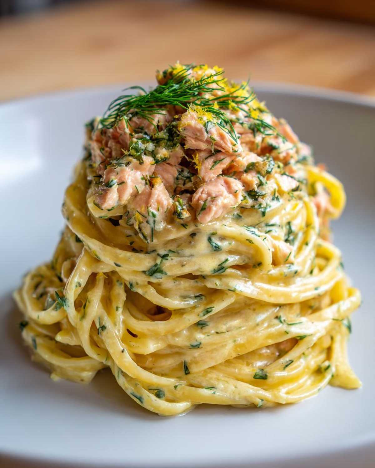 Zbliżenie na porcję makaronu z łososiem w sosie śmietanowym, udekorowany koperkiem i skórką cytryny.
