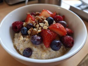 Miseczka pysznej owsianki z owocami: truskawkami, malinami, borówkami i orzechami.