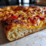 Fragment idealnego ciasta na pizzę domową z widocznymi pęcherzykami powietrza i złocistą skórką.