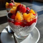 Pudding chia z owocami: warstwy nasion chia, dżemu truskawkowego i świeżych owoców w szklance.