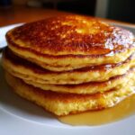 Stos puszystych pancakes amerykańskich polanych syropem na białym talerzu.