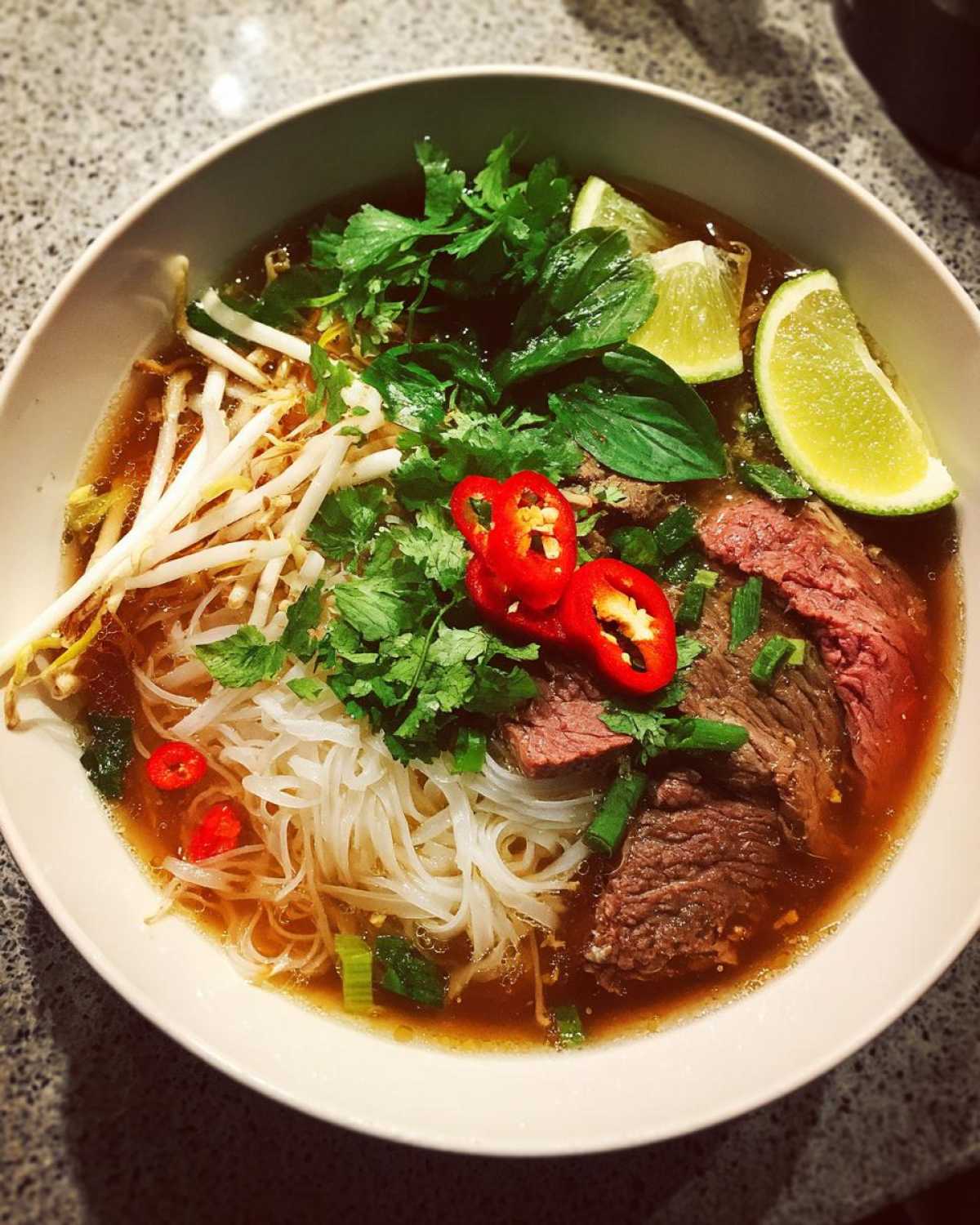 Miseczka aromatycznej zupy pho (wietnamska) z cienkimi plastrami wołowiny, makaronem ryżowym, kiełkami fasoli, kolendrą i chili.