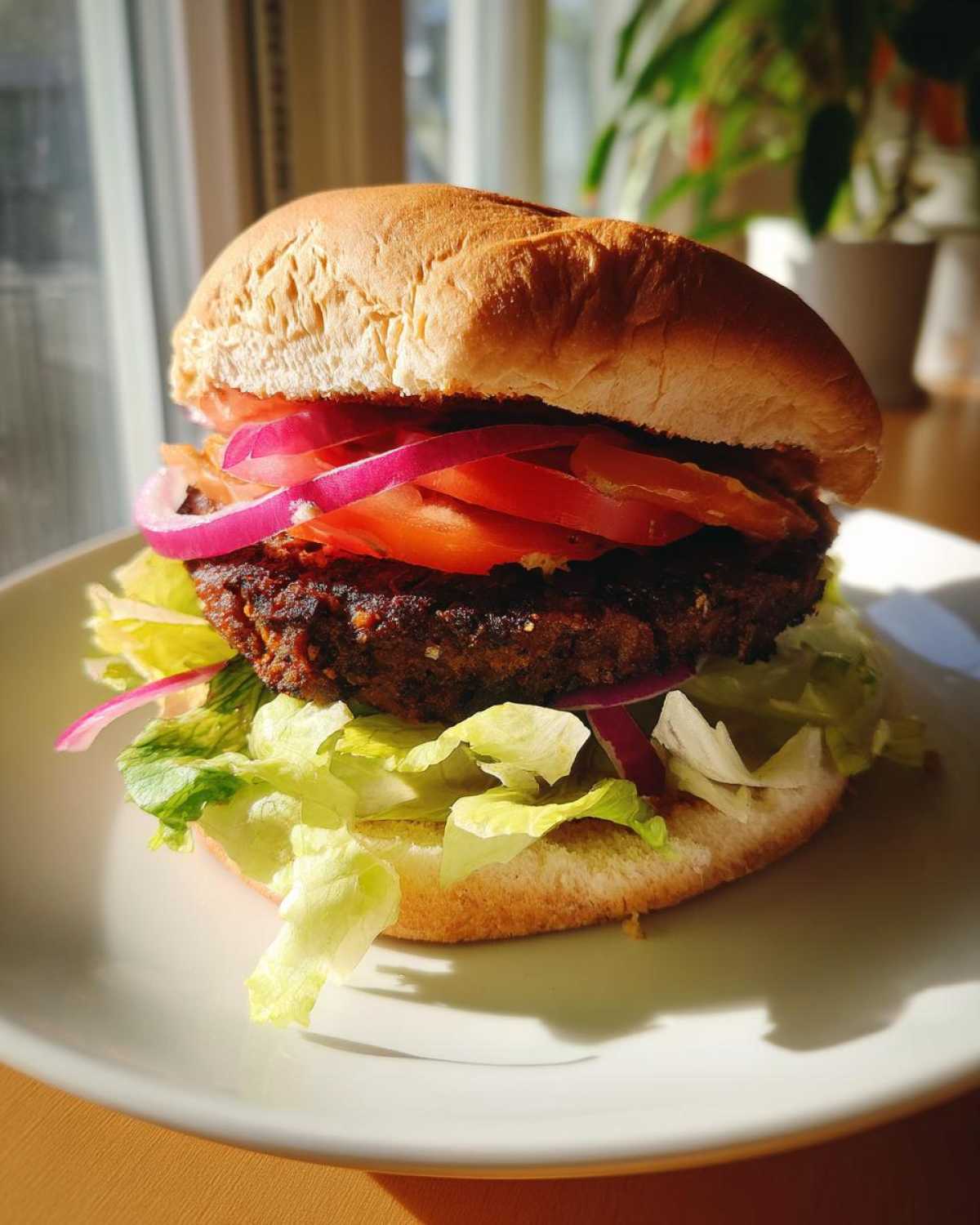 Zbliżenie na gotowy burger sojowy z sałatą, pomidorem i czerwoną cebulą na białym talerzu.